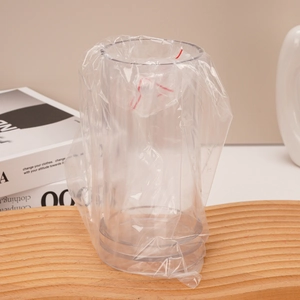 Close-up of a clear cylindrical acrylic candle mold with plastic bag lining on a wooden base