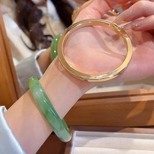 Close-up of polished gold flat bangle and translucent green resin jade-style bracelet