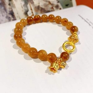 Dettaglio del bracciale di perle citrine con ciondolo mughetto dorato e accenti in metallo