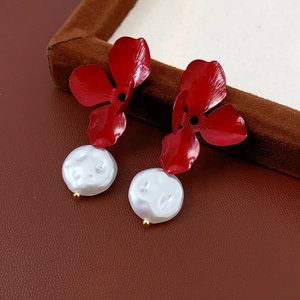 Detailed macro view of red metallic flower earrings with elegant white pearl droplets