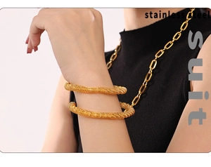 Detailed close-up of golden stainless steel spiral textured bangles on woman wrist