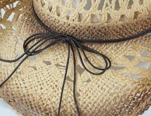 Dettaglio di un cappello di paglia con trama intrecciata e fiocco decorativo marrone