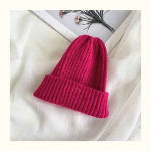 Close-up of pink knitted beanie with vertical ribbed texture on white linen background