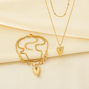 Detail view of double-layered gold heart necklace and chunky chain bracelet on beige cloth