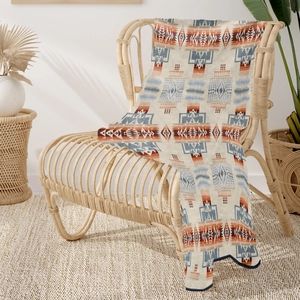 Detail of bohemian geometric flannel blanket draped over a rattan chair in a cozy room