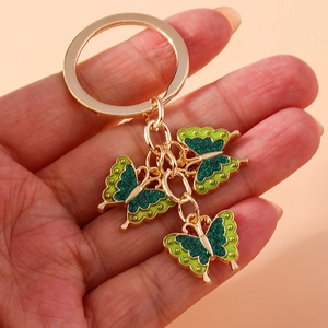 Close-up of golden keychain with three glittery green butterfly pendants held in hand