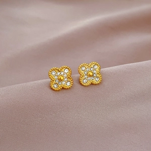 Macro shot of gold-plated clover stud earrings with sparkling white crystals on purple silk