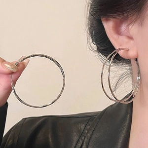 Detail of layered silver hoop earrings with diamond accents worn by a model for scale