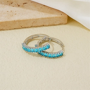 Macro detail of silver hoop earrings with rectangular blue crystals on a stone surface