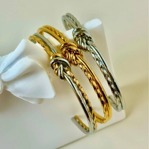 Detailed view of gold and silver knot bangles with twisted texture on minimalist stands