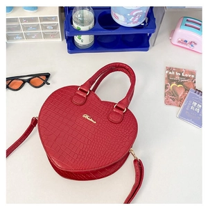 Détail du sac à main rouge en forme de cœur avec texture crocodile et logo en métal doré