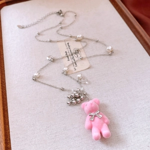 Close-up of pink flocked bear pendant with elegant pearls and silver bow on long chain