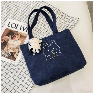 Detail of dark blue corduroy tote bag featuring white rabbit embroidery and plush charm
