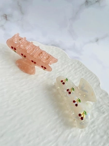 Close-up of pink and white acetate hair claws with sparkling red rhinestone cherry motifs