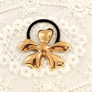 Detailed close-up of golden metallic star flower hair tie on white lace background