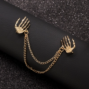Detailed close-up of golden gothic skull hand collar pin with double metal chains