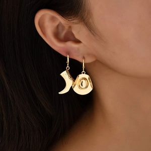 Golden western cowboy boot and hat asymmetric drop earrings worn by a model