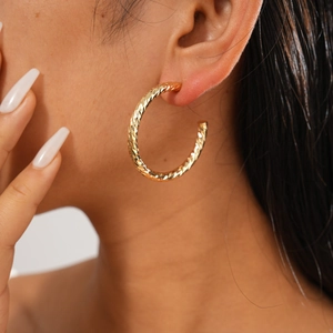Close-up of golden textured geometric hoop earring on model showing fine metal details