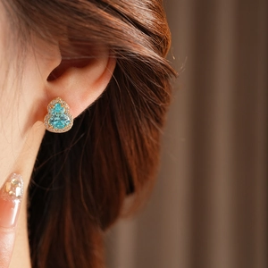 Macro view of gold-plated gourd earrings with a blue gemstone and sparkling zircon accents