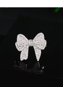 Detailed close-up of a silver bow brooch with sparkling cubic zirconia on black mirror