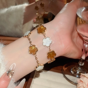 Détail de bracelets fleurs dorés superposés avec pétales en émail sur le poignet du modèle