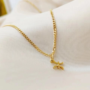 Close-up of a gold Pisces zodiac pendant on a fine stainless steel chain on fabric