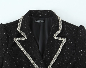 Close-up of black tweed jacket neckline showing silver sequins and woven trim texture