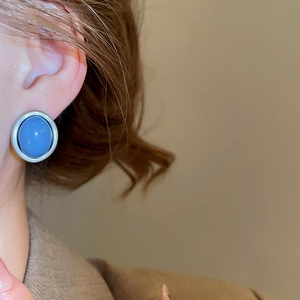 Close-up of blue gemstone stud earrings with silver metal frame on an earlobe