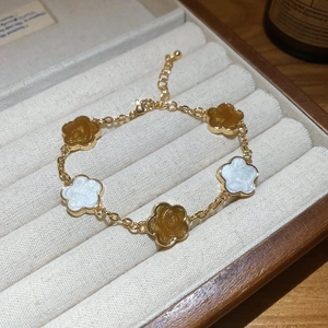 Détail d'un bracelet fleuri doré avec des breloques en émail blanc et ambre poli