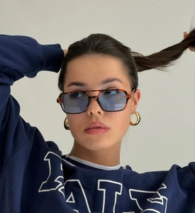 Close-up of tortoise sunglasses with blue lenses and chunky gold hoop earrings