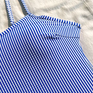 Detail of blue and white striped ribbed fabric and thin shoulder strap of a bikini top