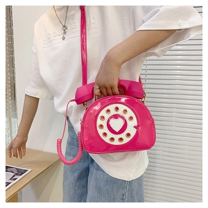 Detail view of pink vintage telephone shaped crossbody bag with heart dial and spring handle