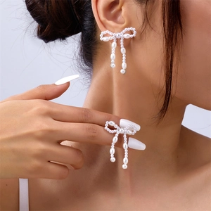Detail of beaded bow earrings with long faux pearl tassels shown on a model