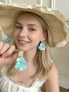 Close-up of blue petal-shaped handmade resin earrings on a model with a straw hat