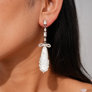 Détail de boucles d'oreilles avec nœud et pendentif goutte blanche et zircons