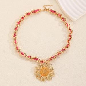 Close-up of golden chain necklace with pink braided rope and sunflower pendant detail