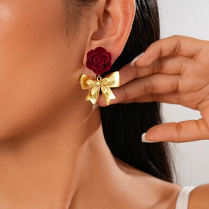Primo piano di modella con orecchini a fiocco dorati e rose in velluto rosso scuro