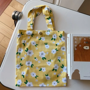 Detail of yellow floral canvas tote bag featuring a secure metal button closure