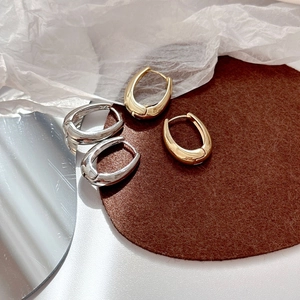 Macro detail of polished gold and silver U-shaped hoop earrings on textured felt background