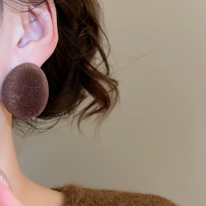 Vue macro de boucles d'oreilles ovales floquées marron portées pour un style d'hiver