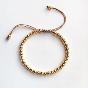 Detail of adjustable gold bead woven bracelet with brown nylon cord on white background