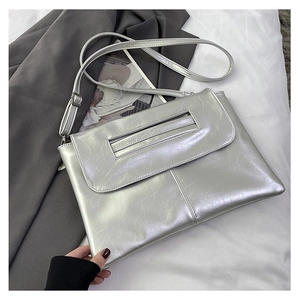 Detail of silver textured leather clutch showing rectangular cutout handle and shoulder strap