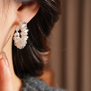 Close-up of irregular hollow geometric silver hoop earrings with diamond textured weave