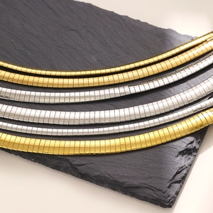 Gold and silver flat snake bone chain necklaces displayed on a rustic grey slate stone