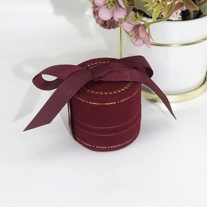 Detail of round burgundy velvet ring box featuring a decorative grosgrain ribbon bow