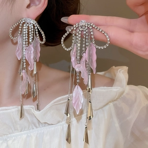 Detail of bow-shaped earring with pink resin leaves and long rhinestone tassels on a model