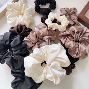 Close-up of assorted satin silk scrunchies in earth tones like mocha, black, and white
