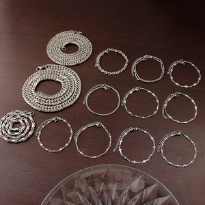 Variety of silver stainless steel necklaces and bracelets in different link styles on wood