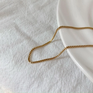 Close-up of a golden stainless steel box chain necklace on white fabric and porcelain