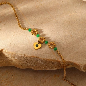Detailed close-up of gold chain bracelet with green beads and heart charm on stone